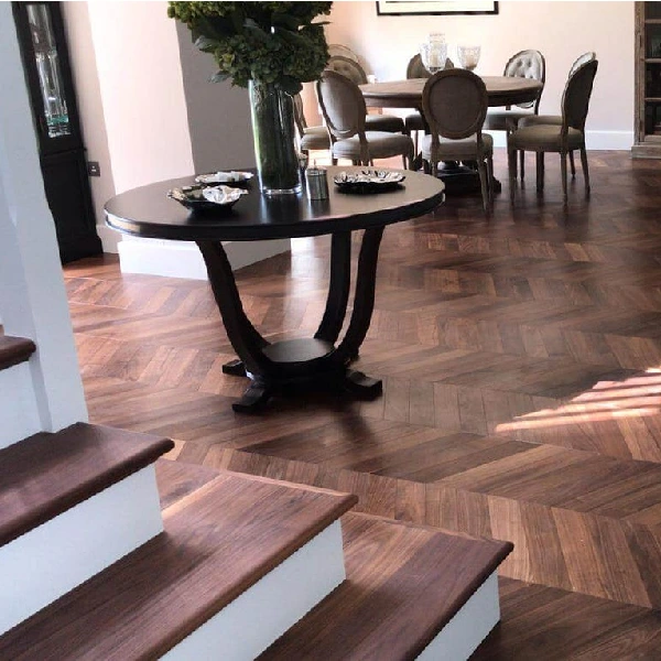 Chevron pattern walnut wood flooring in a dining room with a dark table.